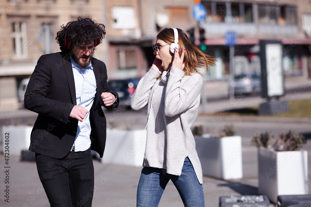 Young business colleagues dancing together with headphones after work. Happy friends jumping and fooling around outdoors Young business colleagues dancing together with headphones after work. Happy friends jumping and fooling around outdoors