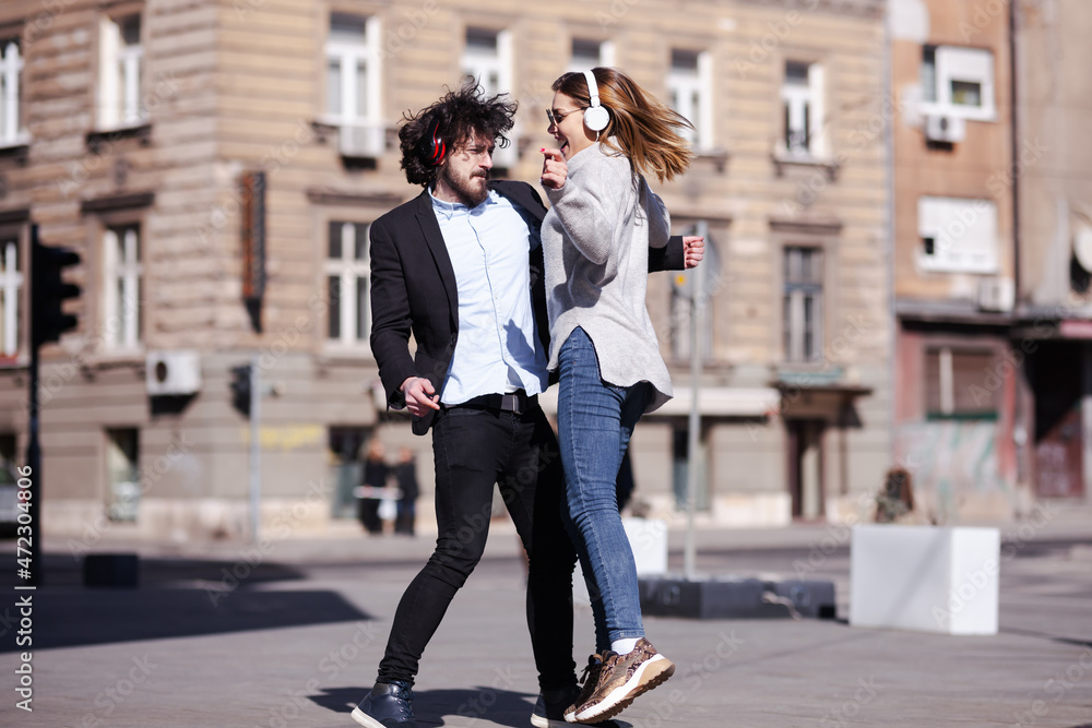 Young business colleagues dancing together with headphones after work. Happy friends jumping and fooling around outdoors