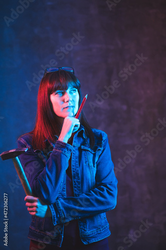 Woman illuminated by neon light holds hammer and pencil in her hands. Renovation and design concept with space for text.