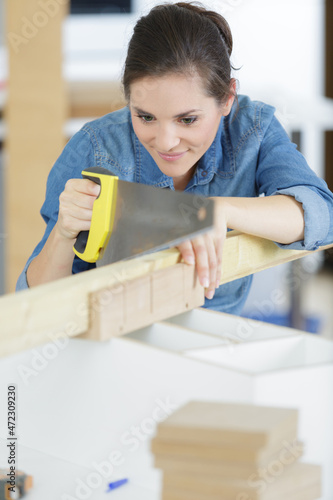 young craftswoman cutting a wooden board with a handsaw indoors photo