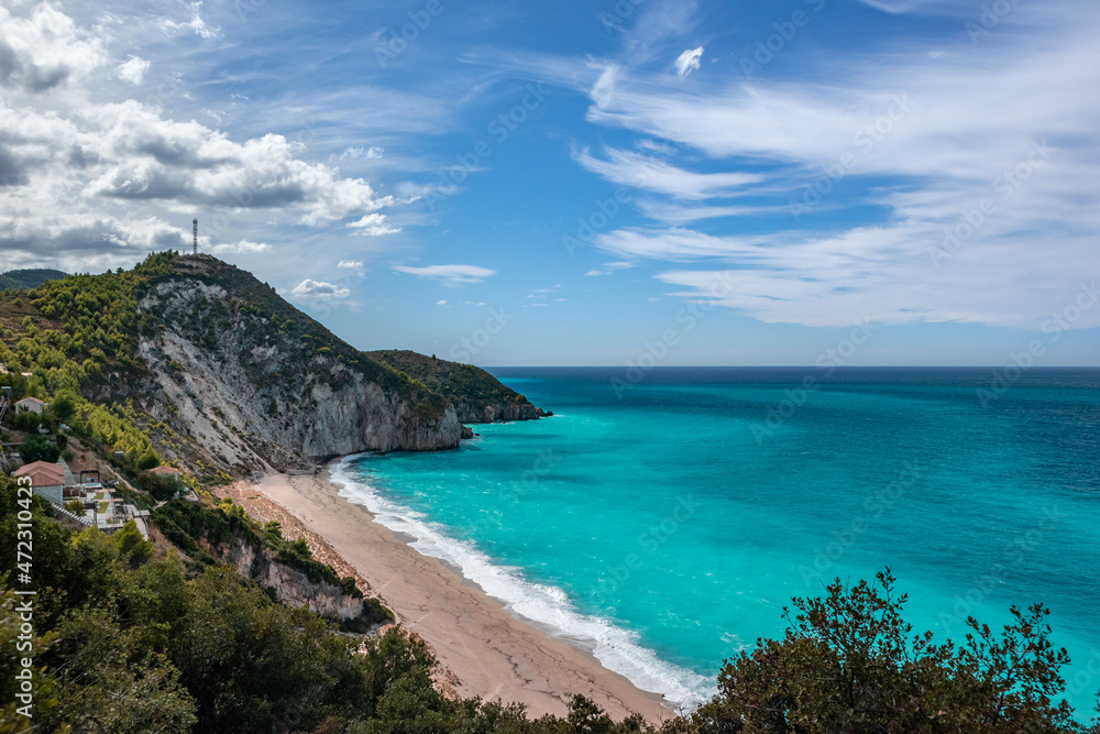 Greek summer Mylos sandy beach with azure vibrant waves and green hills on coast of Lefkada island in Greece. Summer vacation travel to Ionian Sea