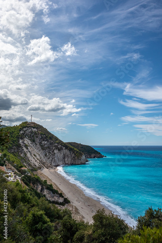 Mylos sandy beach with azure vibrant stormy waves and clouds on coast of Lefkada island in Greece. Summer nature travel to Ionian Sea. Vertical