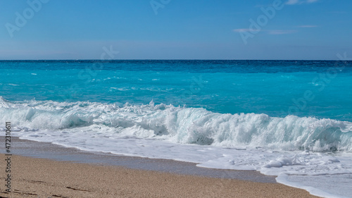 Blue vibrant breaking waves on shore of Greek island with blue sky. Sandy beach in Greece. Summer nature travel to Ionian Sea