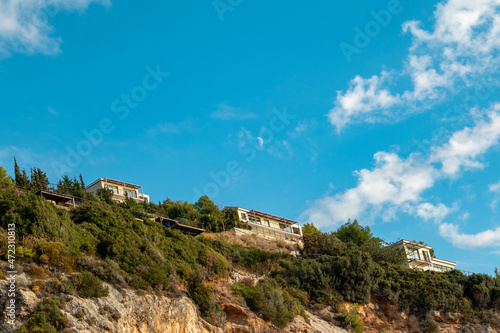 Scenic vibrant landscape with Greek recreation villa houses on green high hills on blue scenic sky with clouds and young moon on Lefkada island  Greece. Travel in summer