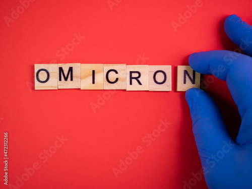 Omicron variant replaces Delta. Emergence of new dangerous strain of coronavirus COVID-19 Omicron. Blue gloves on hand. Words omicron on colored red background