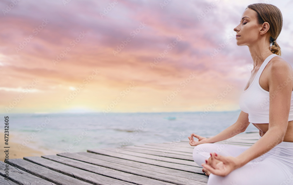 Yoga and meditation. Closeup of young woman in lotus pose on wooden deck with sea view.
