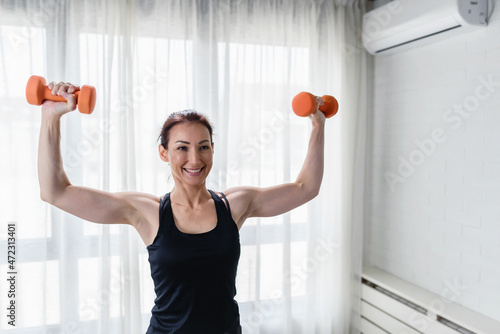Smiling young woman working out with dumbbells at home. Daily exercise routine