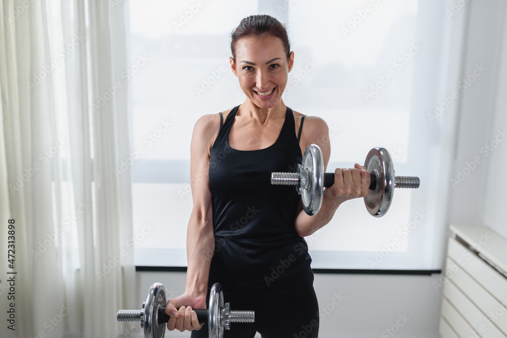 Smiling young woman working out with dumbbells at home. Daily exercise routine Smiling young woman working out with dumbbells at home. Daily exercise routine