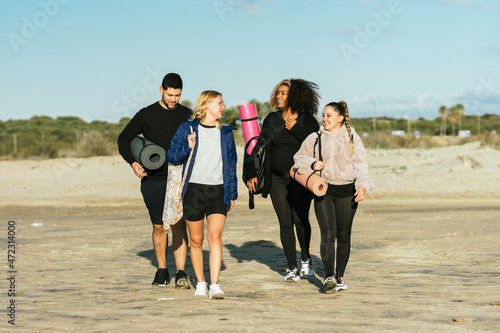 Multiethnic group walking on the beach with yoga mats and bags