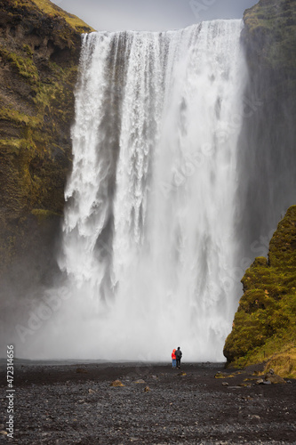 A couple standing next to the famous Skogafoss waterfall in Skogar, southern Iceland.