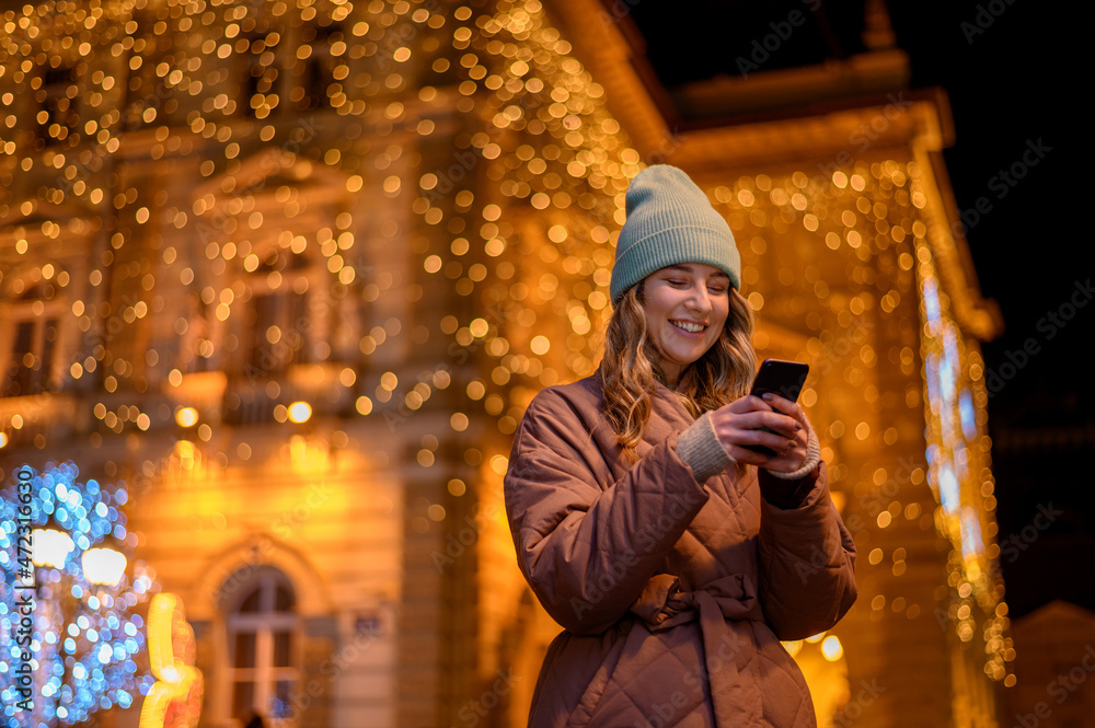 Young woman using a smartphone outside with the decorative christmas lights in the background
