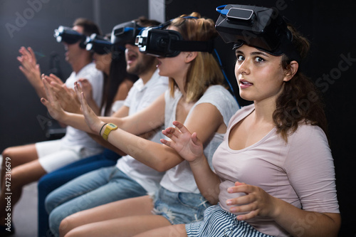 Young italian scared girl on virtual reality attraction sitting with another people