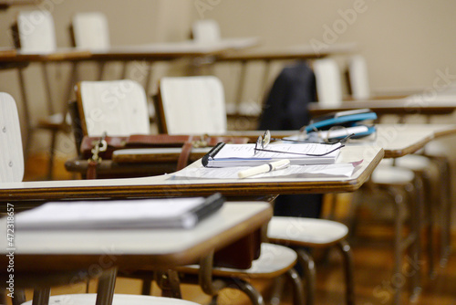 desks in a classroom with notebooks and pens, with no people occupying the seats.