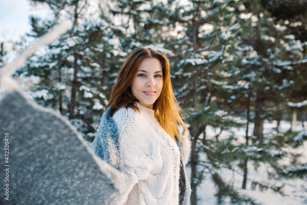 Beautiful smiling young woman in wintertime outdoor. Snowy winter park. Portrait of a red-haired girl in a woolen sweater and scarf. Beautiful smiling young woman in wintertime outdoor. Snowy winter park. Portrait of a red-haired girl in a woolen sweater and scarf.