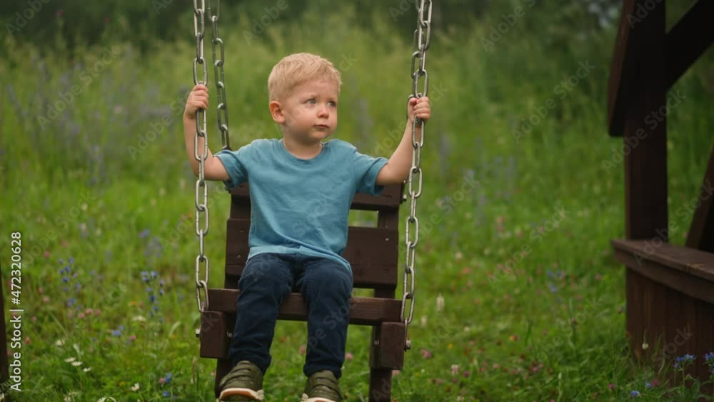 Blond little boy kid plays handmade swings with chains spending time on ground with grass on nasty spring day at countryside slow motion Blond little boy kid plays handmade swings with chains spending time on ground with grass on nasty spring day at countryside slow motion