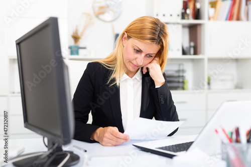 Frustrated businesswoman working alone with papers and laptop in business office
