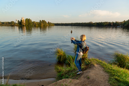 The girl on the bank of the pond takes pictures on the phone. Moscow, Stroginskaya Poima
