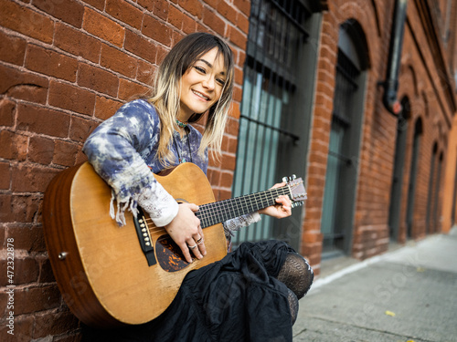 Young female Indigenous artist playing guitar outdoors photo