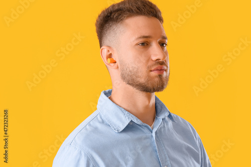 Young man with ear plug on yellow background