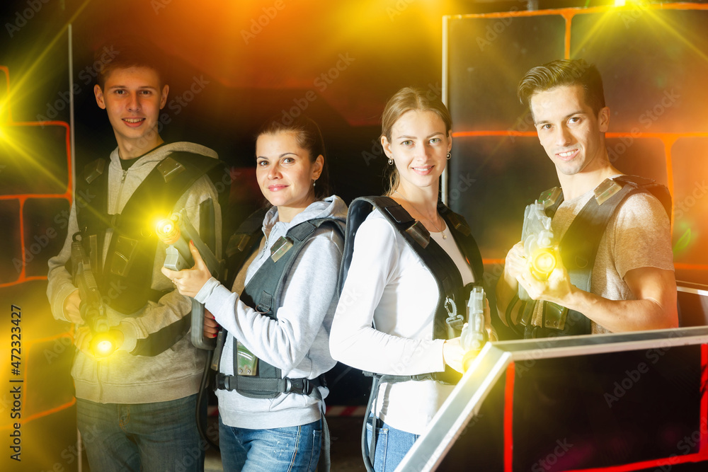 Group of adult friends with laser guns having fun on dark lasertag gaming arena