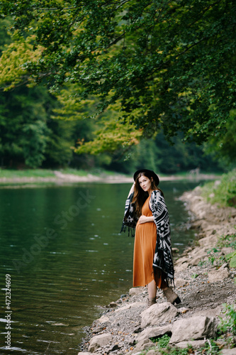 Fototapeta Naklejka Na Ścianę i Meble -  Pregnant woman stands on the shore of a lake in a green forest