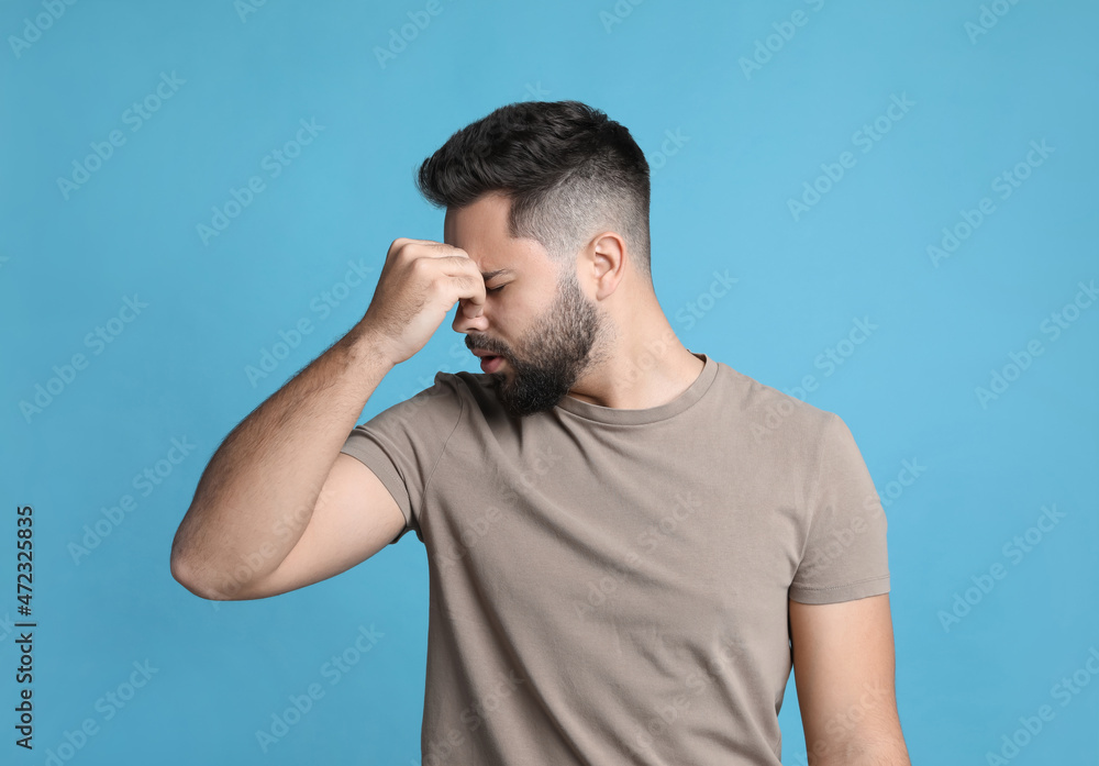 Young man suffering from headache on light blue background Young man suffering from headache on light blue background