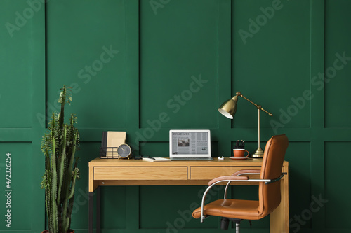 Modern workplace with laptop near green wall in room