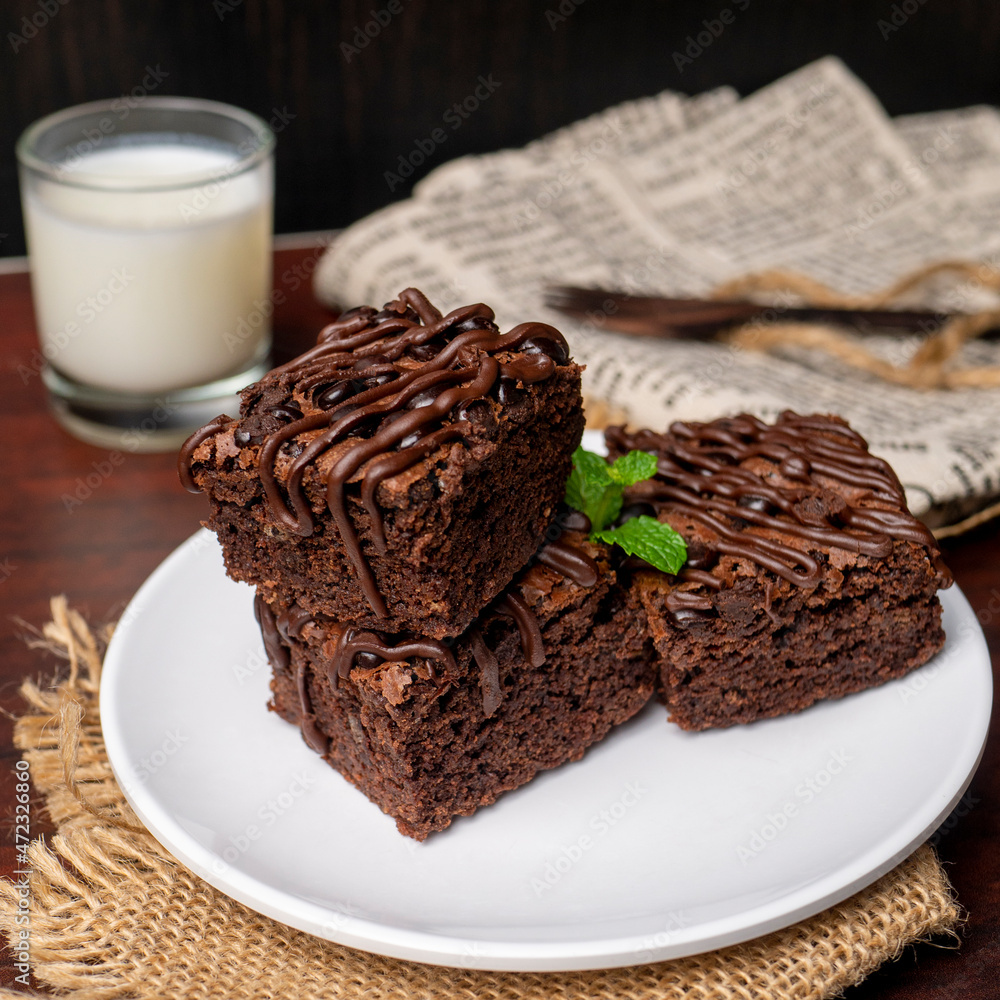 Chocolate Brownies with a glass of milk on white plate and wooden table Chocolate Brownies with a glass of milk on white plate and wooden table