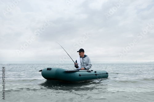 Man fishing with rod from inflatable rubber boat on river
