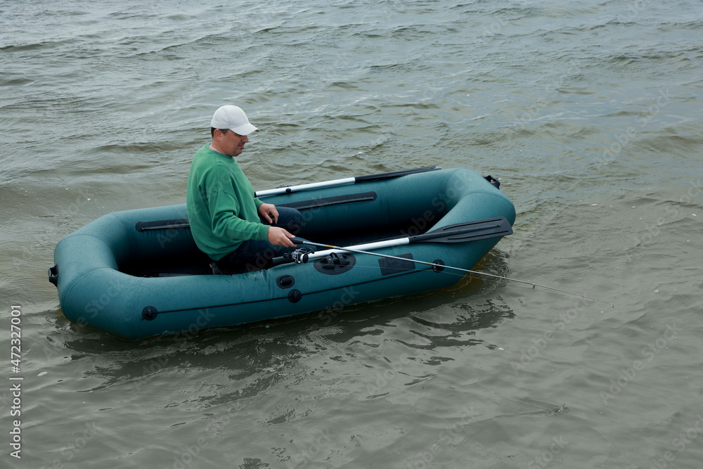Obraz premium Man fishing with rod from inflatable rubber boat on river
