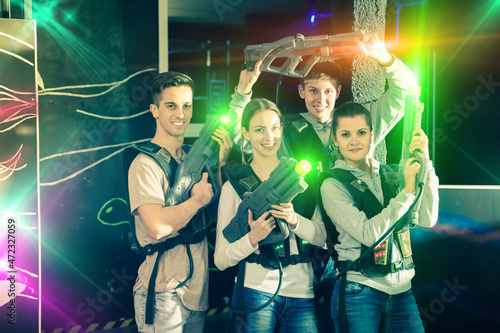 Portrait of cheerful young friends with laser guns during lasertag game on dark lasertag arena