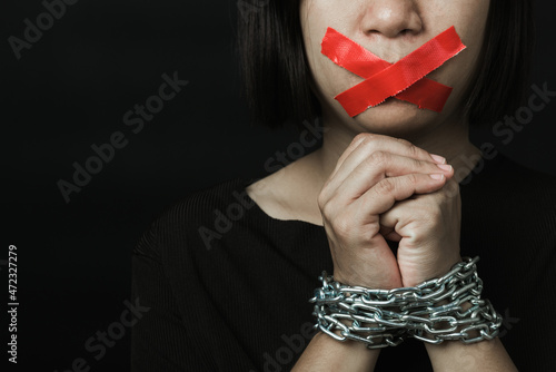 Fotografía Asian woman blindfold wrapping mouth with red adhesive tape and she was hand tethered on black background