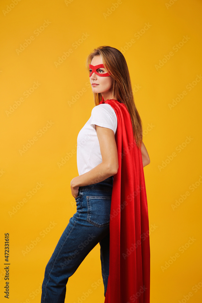 Confident woman wearing superhero cape and mask on yellow background