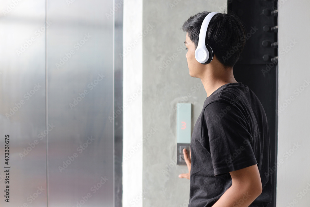 Millennial youth wearing wireless headphones pressing elevator button 
