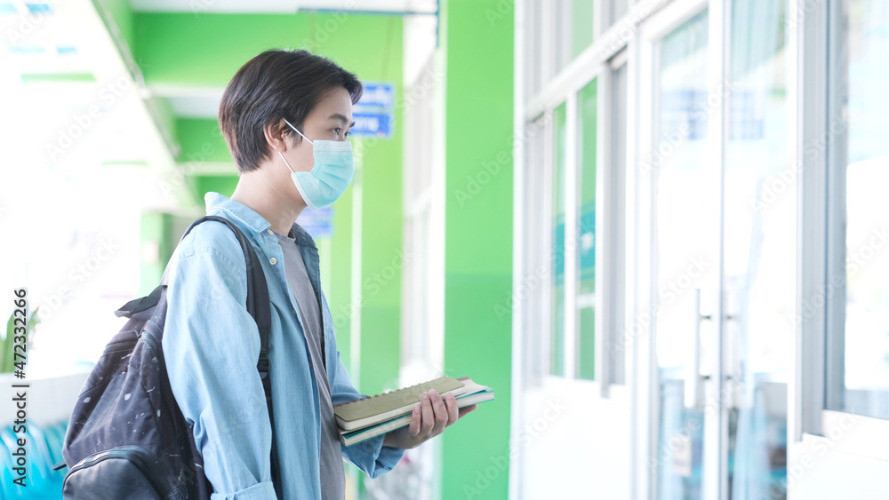Fototapeta premium Young asian campus student man wearing protection mask while walking in campus, coronavirus prevention in university, social distancing