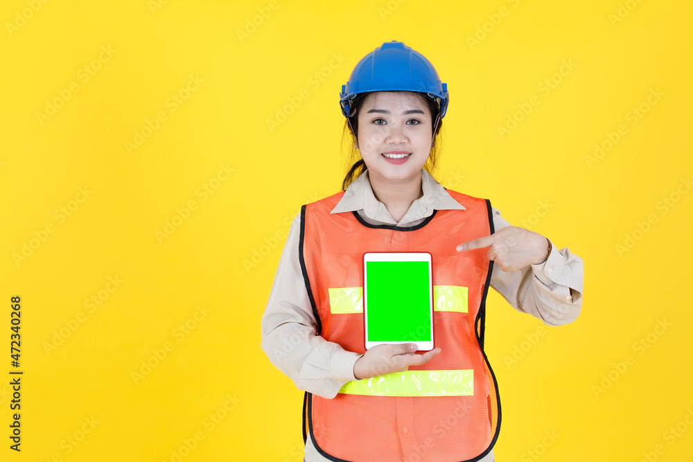Portrait studio shot Asian female professional engineering foreman manager in hard helmet and reflective safety vest smiling look at camera checking inventory stock from tablet on yellow background Portrait studio shot Asian female professional engineering foreman manager in hard helmet and reflective safety vest smiling look at camera checking inventory stock from tablet on yellow background