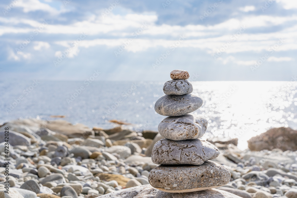 A pyramid of round stones (ladza) close-up on a rocky beach on a blurred background of a sunny path on a restless sea surface A pyramid of round stones (ladza) close-up on a rocky beach on a blurred background of a sunny path on a restless sea surface