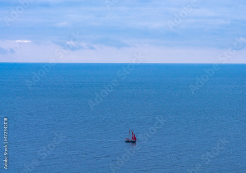 A lonely yacht with scarlet sail sails on the blue sea in the distance in cloudy weather