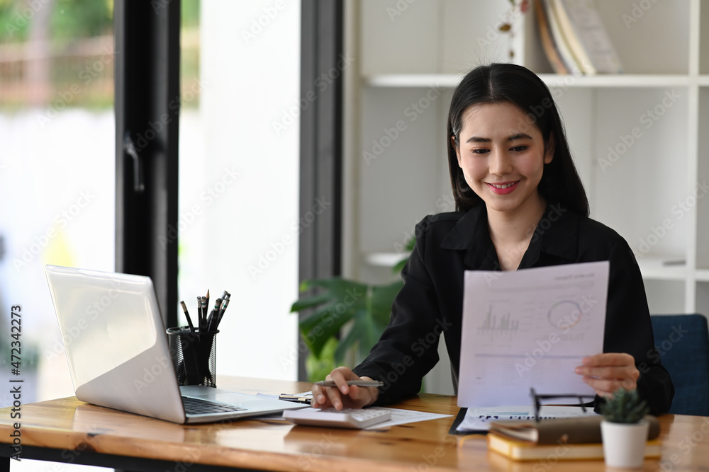 Smiling businesswoman holding document and working with laptop computer. Smiling businesswoman holding document and working with laptop computer.
