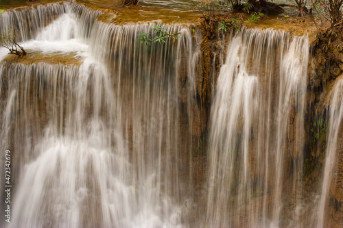 The close-up of a waterfall in layers with brown rock and trees from Thailand.