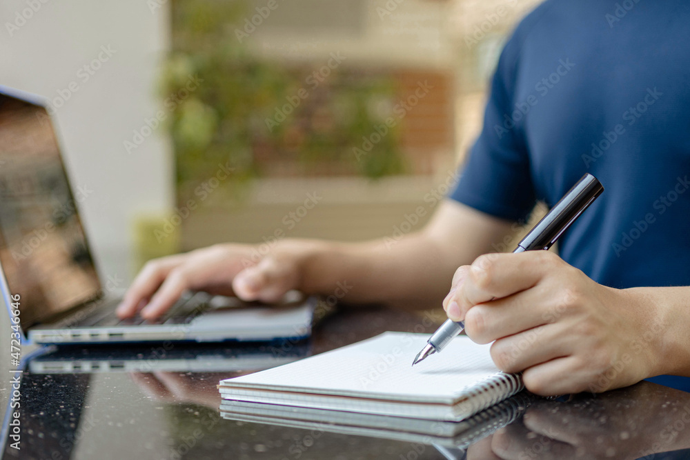 Online studying concept the man who is working from home attempting to write the meeting report down while online meeting of his company is conducting Online studying concept the man who is working from home attempting to write the meeting report down while online meeting of his company is conducting