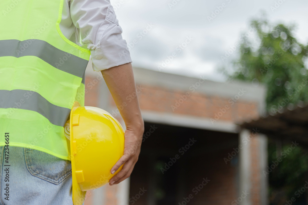 engineer concept The male constructing staff that wears a white top covered with bright lime vest, a black watch, and light blue jeans standing and holding a mustard safety hat engineer concept The male constructing staff that wears a white top covered with bright lime vest, a black watch, and light blue jeans standing and holding a mustard safety hat