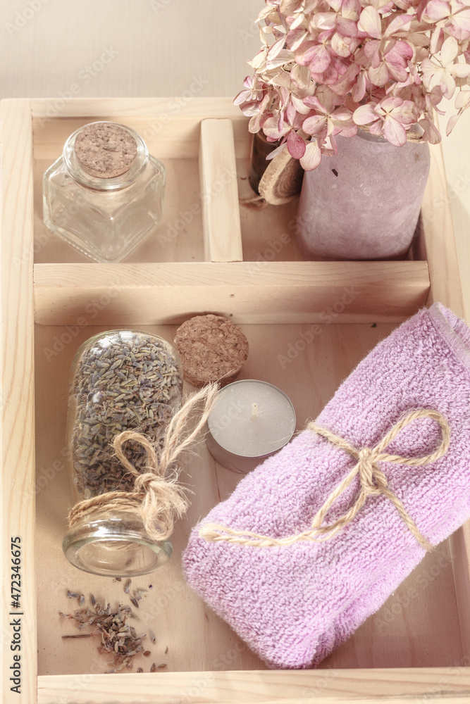 Lilac-colored towel, bottle of dry herbs on a wooden tray.  Herbal spa, Body care, flat lay