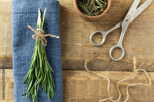 A bunch of fresh rosemary tied with jute cord on a burlap napkin with old scissors on a wooden table. Rustic style. Ultra urban farming. Indoor Gardering. Selective focus. Top view.