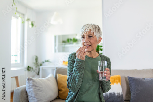 Senior woman takes pill with glass of water in hand. Stressed female drinking sedated antidepressant meds. Woman feels depressed, taking drugs. Medicines at work photo