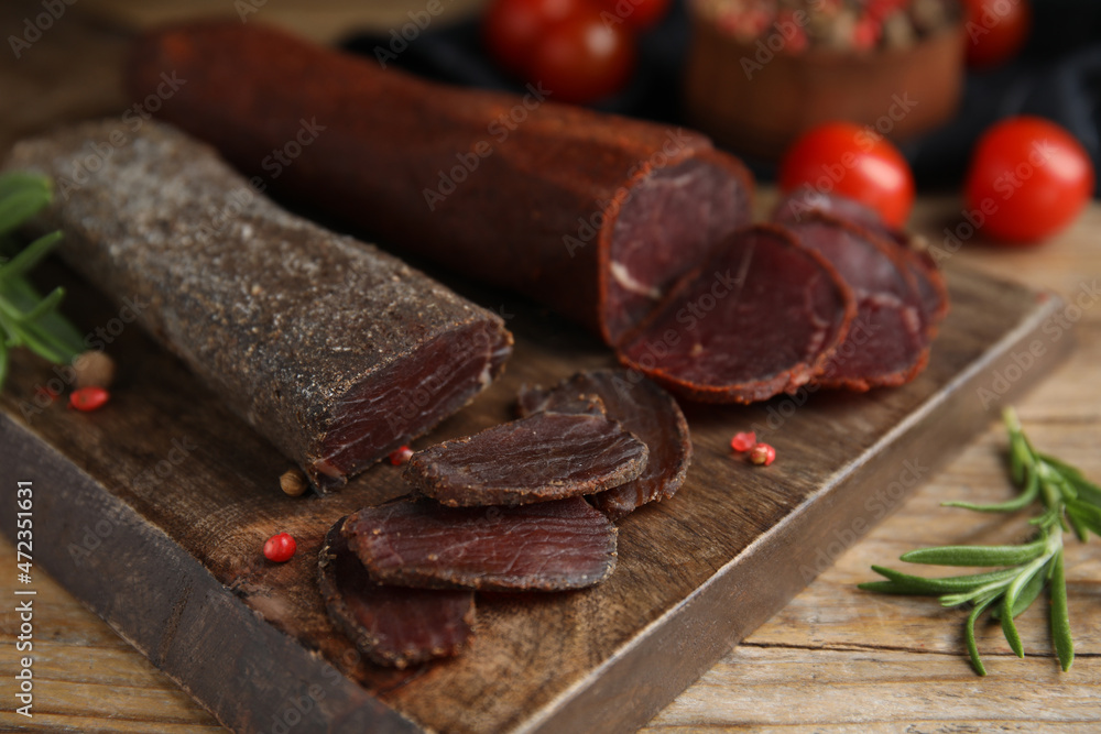 Delicious dry-cured beef basturma with rosemary and peppercorns on wooden table, closeup