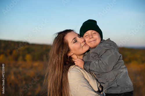 Little caucasian boy giving a hug to his happy smiling mother outdoors close up portrait