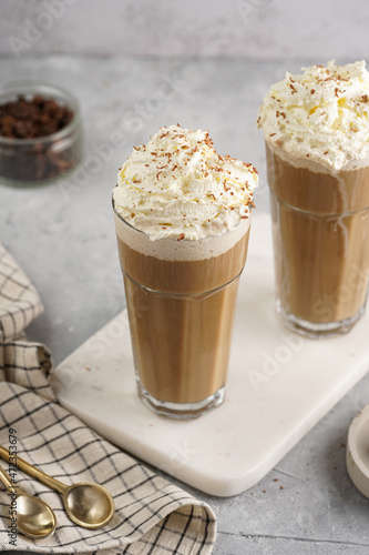 Two tall glasses with cold coffee drink frappe - iced cappuccino with whipped cream on a marble board
