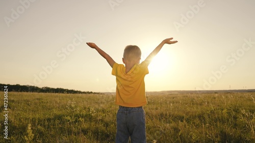 happy child boy prays, spreading his hands to the sides at sunset, kid praying to the sun in sky, pulling helping hand, enjoying freedom outdoors walking in nature in park, inspiring childhood dream