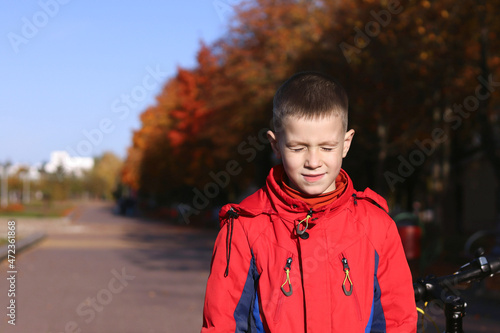 The child closed his eyes from the bright sun, red jacket, autumn day